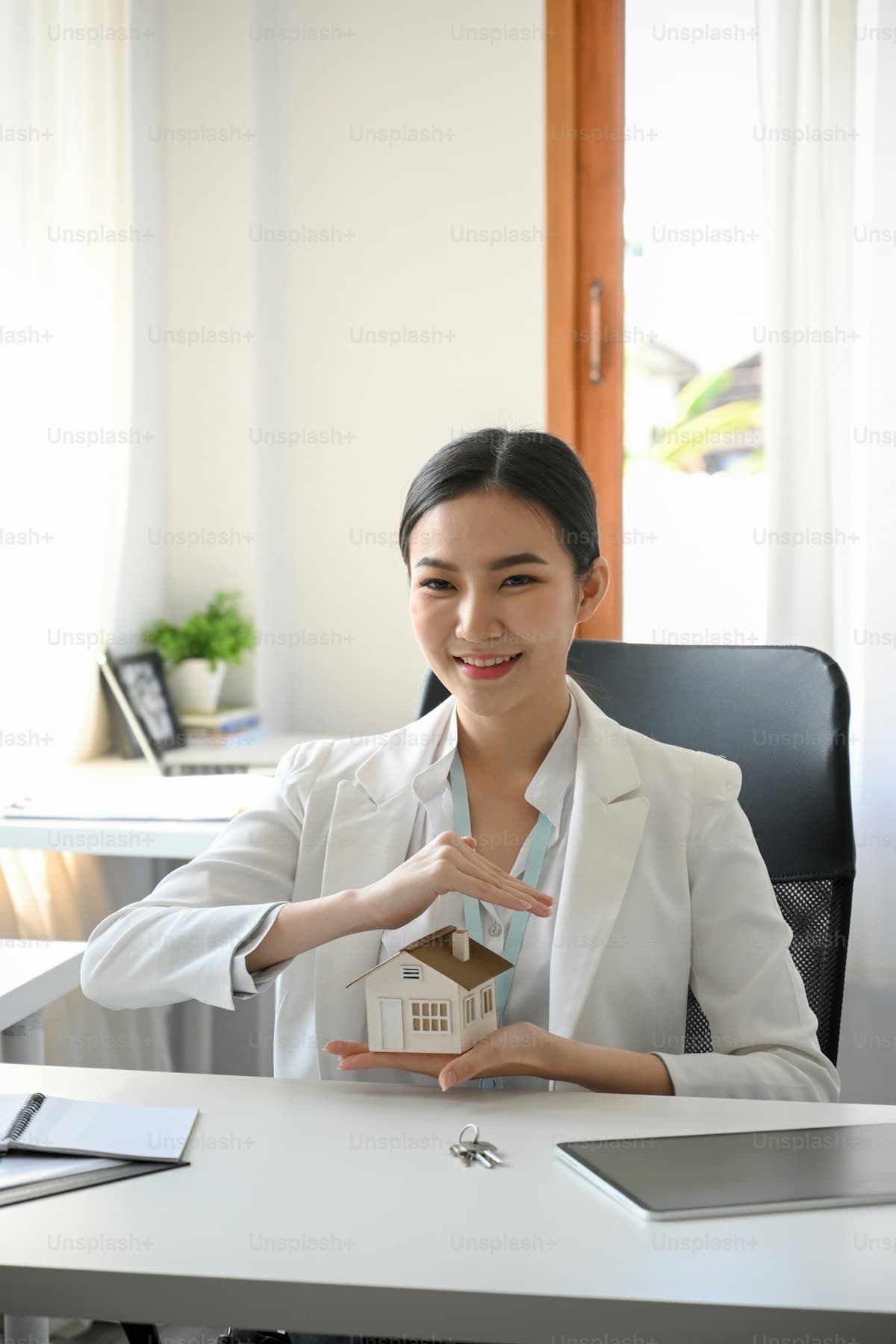 Property manager at a professional office desk reviewing documents beside a miniature house model